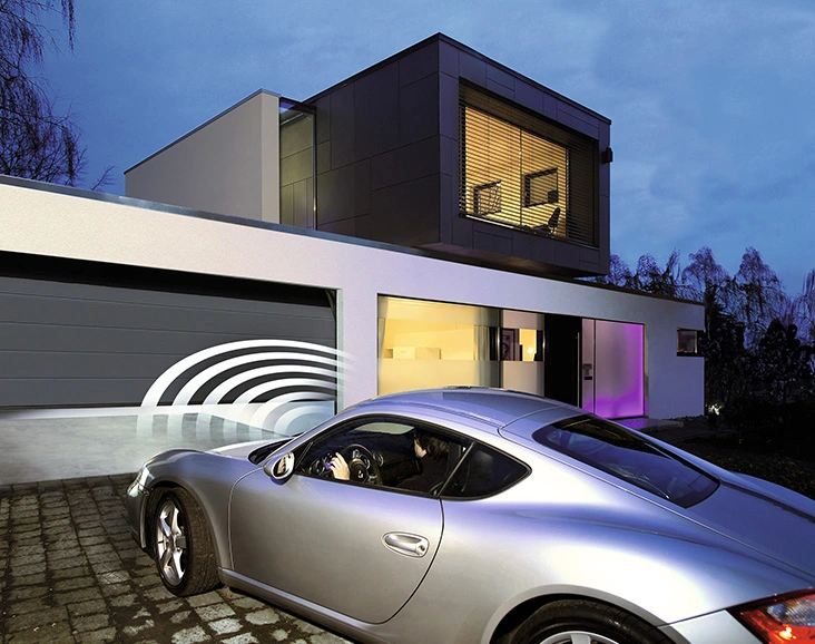 Auto auf Einfahrt eines modernen Hauses im Abendlicht, zielt auf die sich elektrisch öffnende Garage, während Hauslichter und Haustür eine warme Willkommensszene malen.